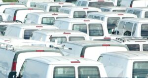A sea of white vans parked closely together, likely a fleet ready for delivery or service jobs, emphasizing the scale of urban logistics and transportation services.